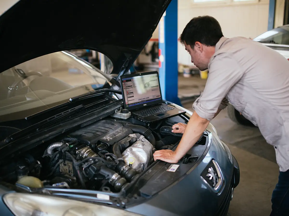 Mechanic using a laptop to run diagnostics on a car engine in the workshop