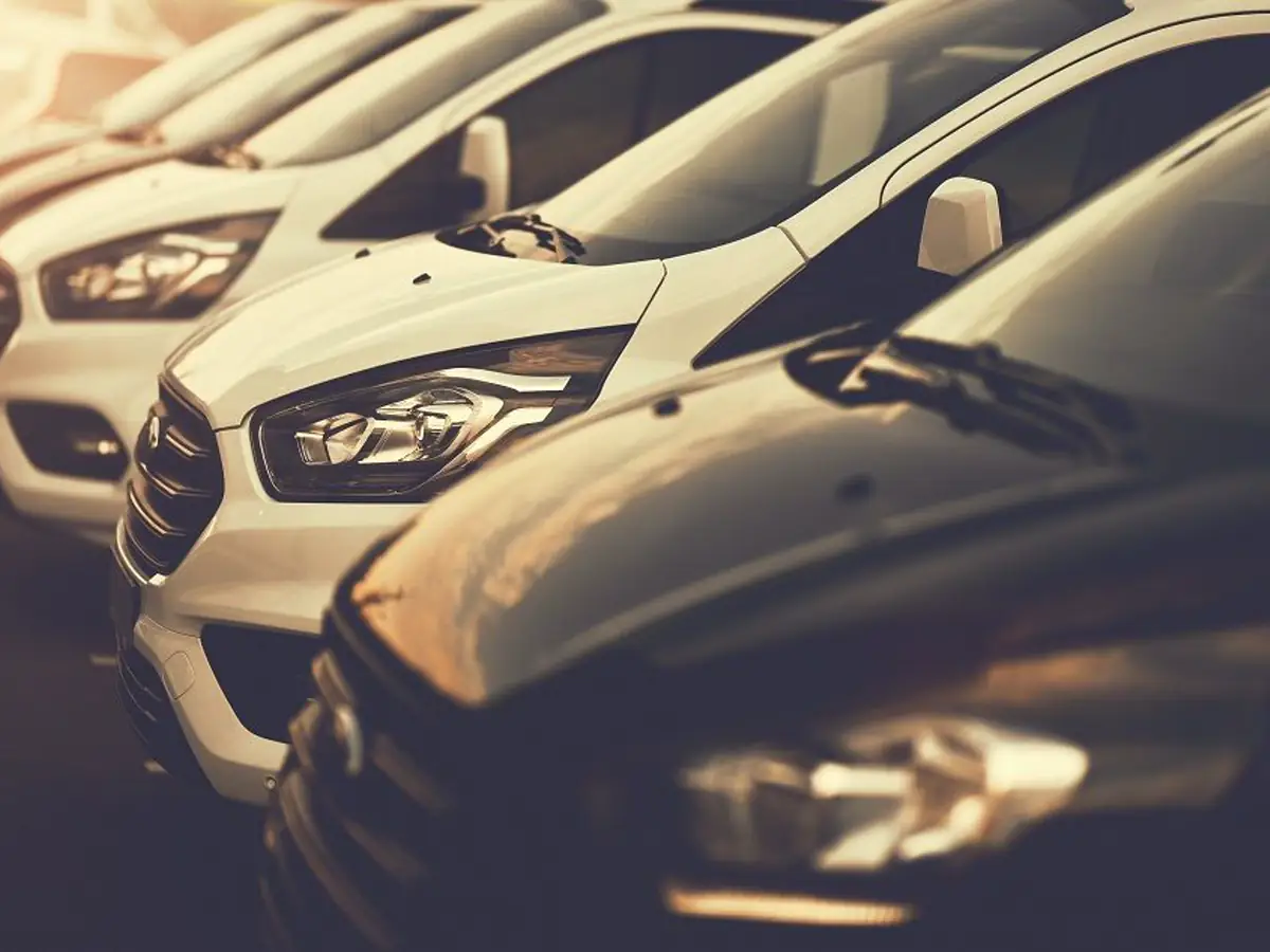 Row of white fleet vans and pickup trucks parked outside a repair shop