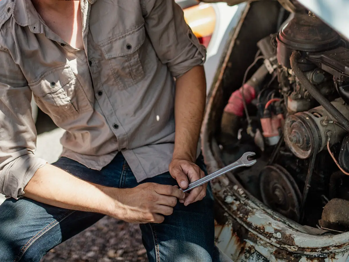 Mechanic kneeling beside an older car engine with a wrench in hand